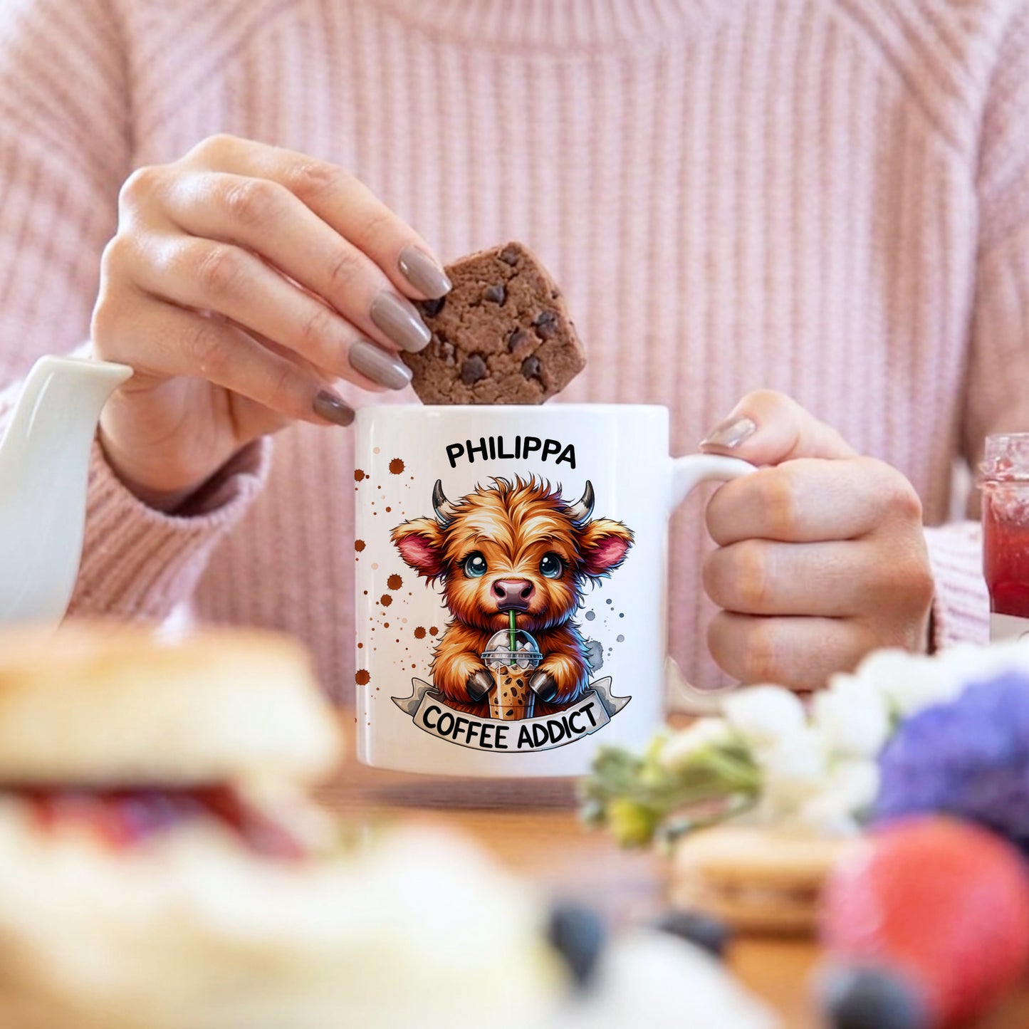 Person holding a mug with a cow illustration and 'Philippa Coffee Addict' text, surrounded by food.