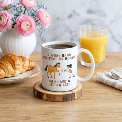Mug with horse and person illustration and text on a table with coffee, juice, and flowers.