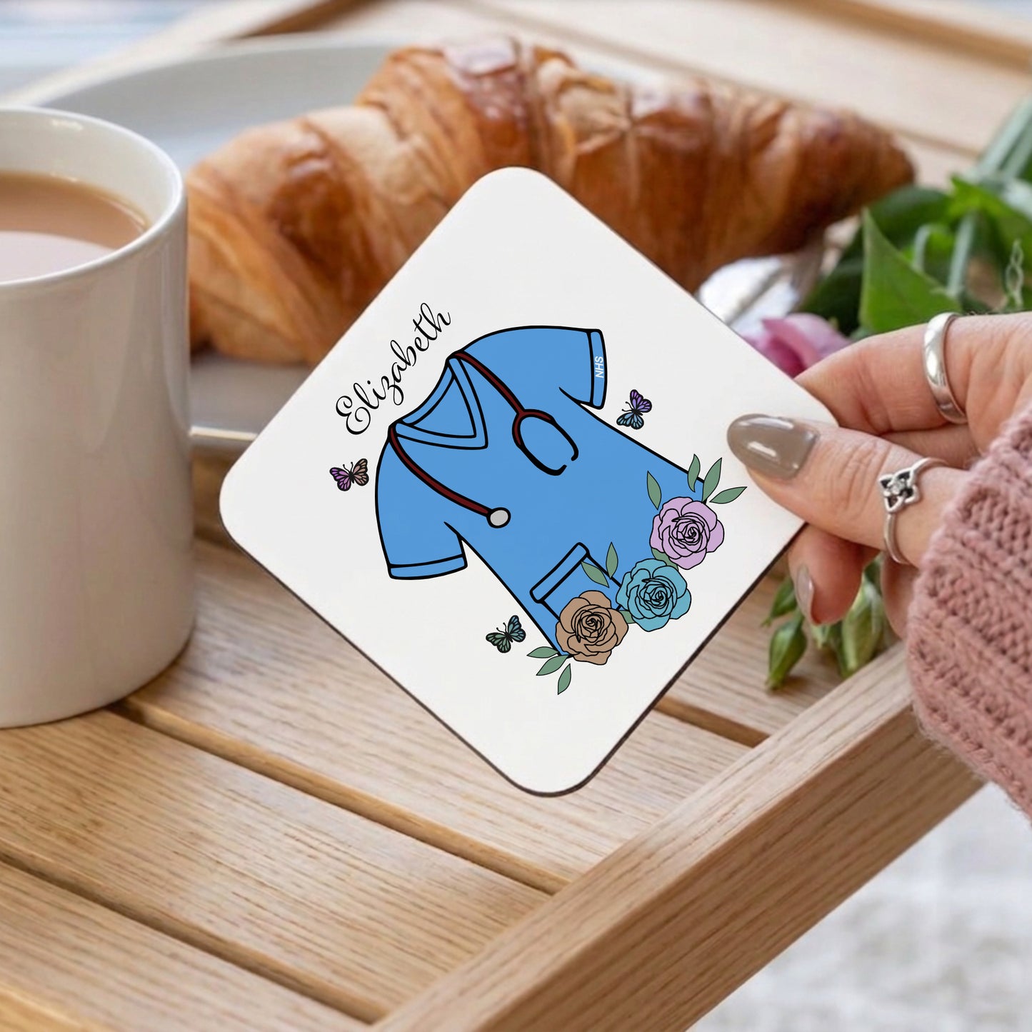 Coaster with medical-themed design held by a hand on a table with coffee and croissant.