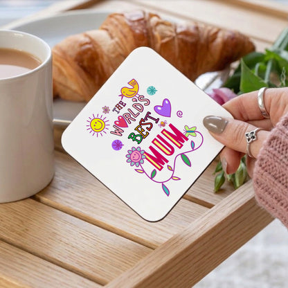 Coaster with 'The World's Best Mum' text held by a hand over a cup of coffee and croissant on a wooden table.