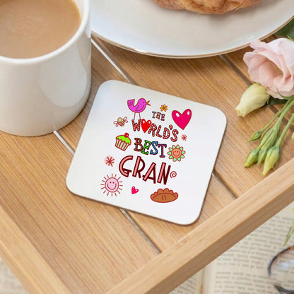 Coaster with 'The World's Best Gran' text on a wooden table with a cup of coffee and flowers.