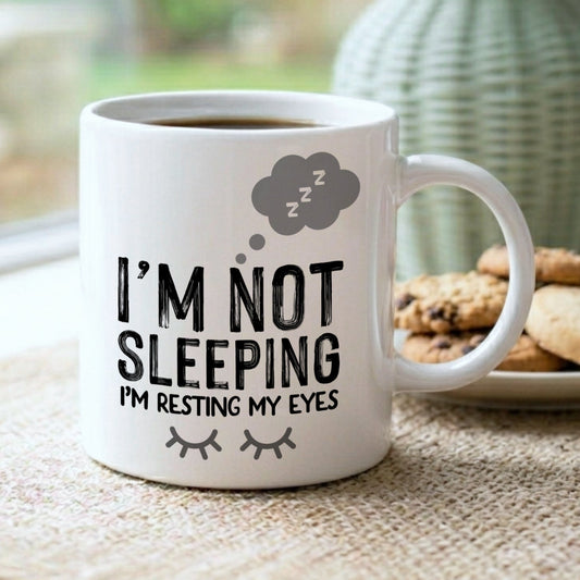 White mug with humorous text on a table with cookies and a vase in the background