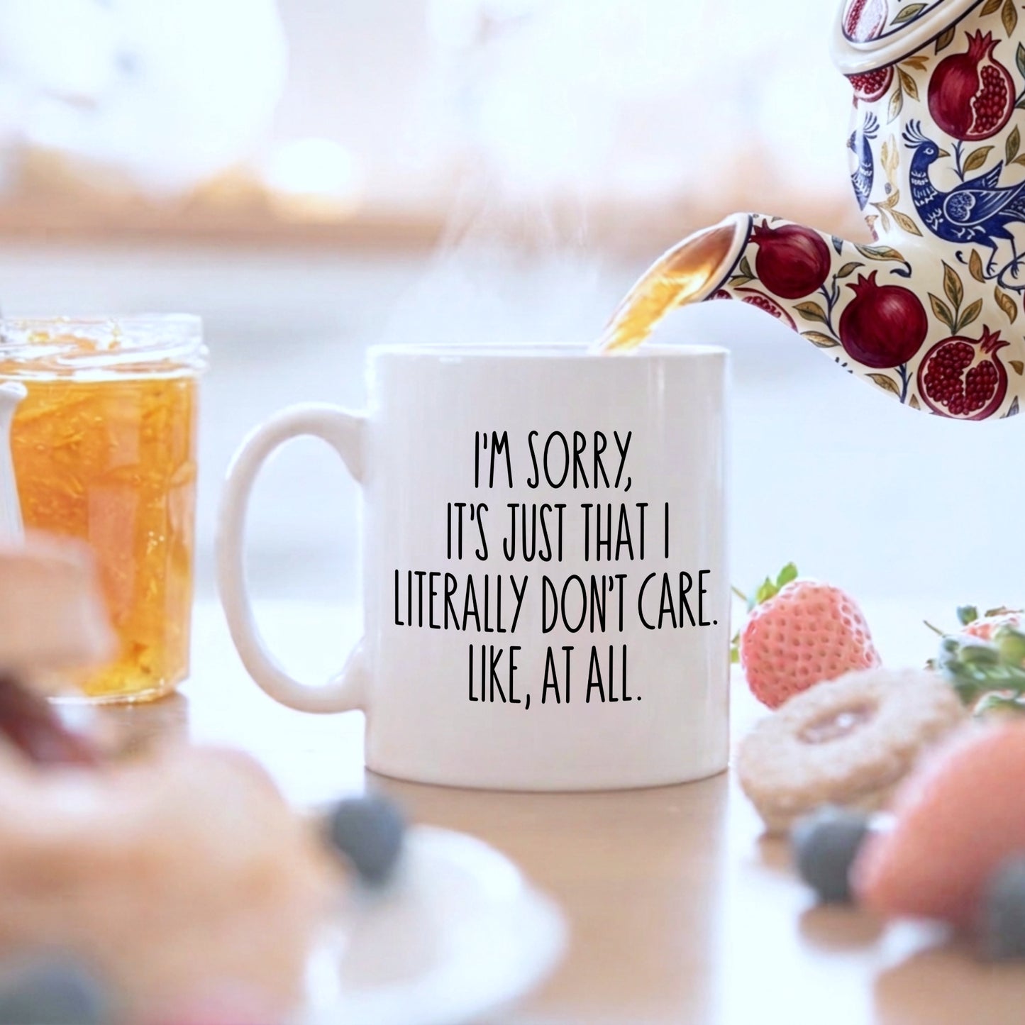 White mug with black text "I'm sorry, it's just that I literally don't care. Like, at all", on a breakfast table having tea poured into it from a teapot
