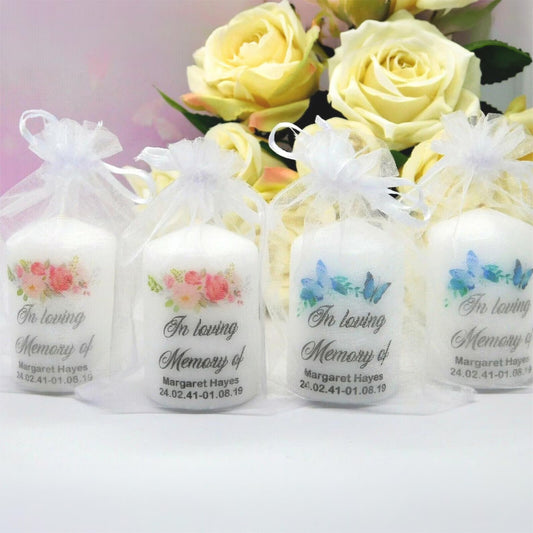 Four white taper candles in clear organza bags with white ribbons, each printed with floral and butterfly designs and the text 'In loving Memory of Margaret Hayes' on a white background with yellow roses behind them.