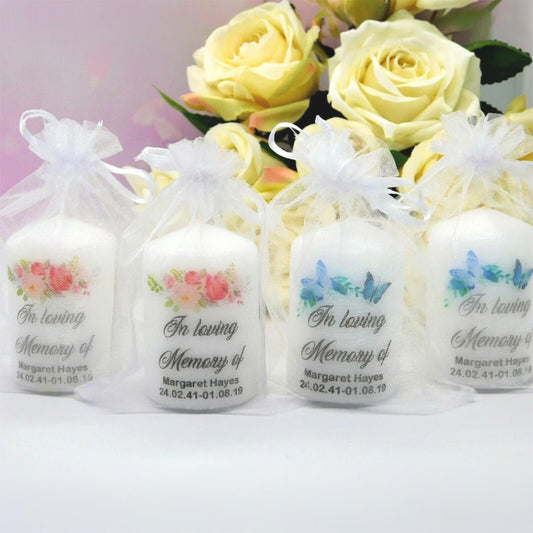 Four white taper candles in clear organza bags with white ribbons, each printed with floral and butterfly designs and the text 'In loving Memory of Margaret Hayes' on a white background with yellow roses behind them.