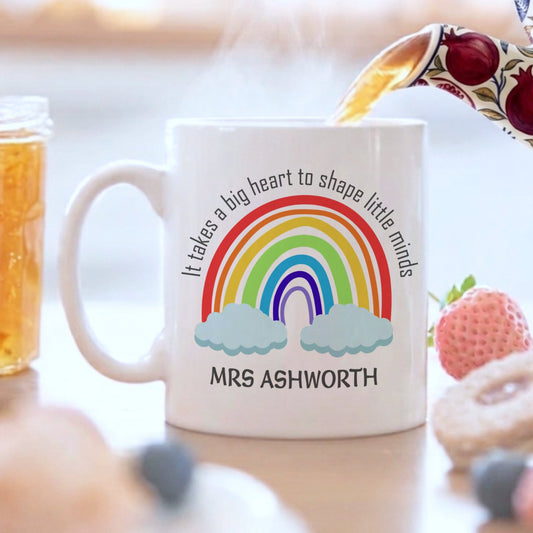 Mug with rainbow design and text being filled with tea, surrounded by snacks on a table.