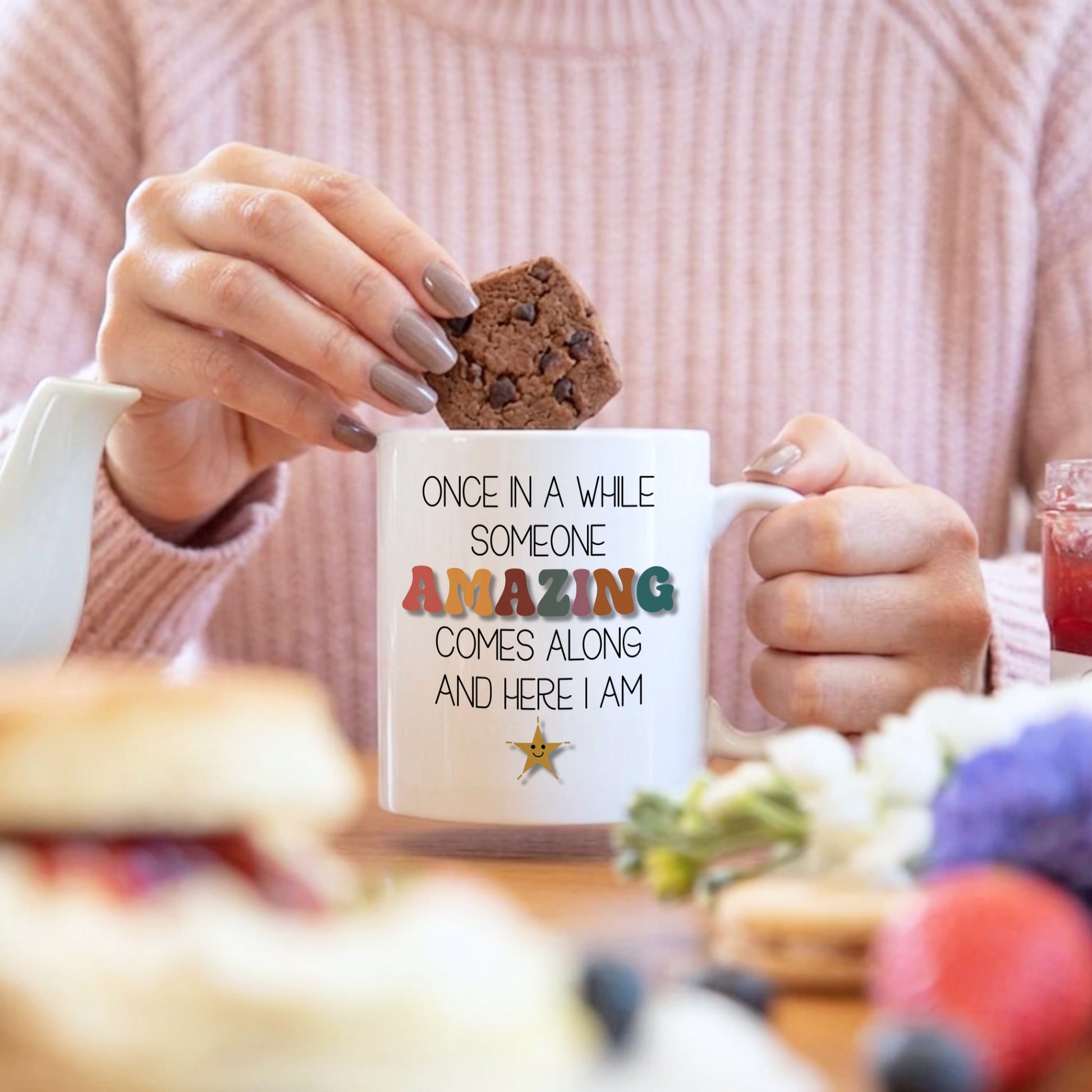 Person holding a mug with a quote and a cookie, blurred background
