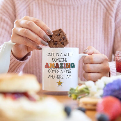 Person holding a mug with a quote and a cookie, blurred background
