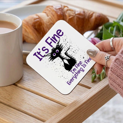 Coaster with 'It's Fine' text and cat illustration on a table with coffee and croissant.