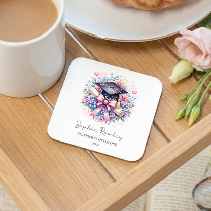 Coaster with graduation design on a wooden table with a cup of coffee and flowers.