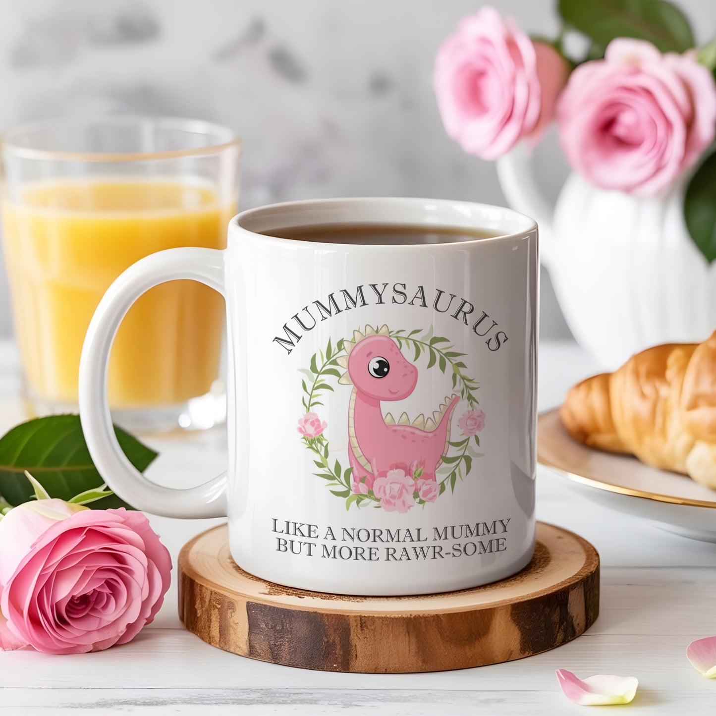 Mug with 'Mummyaurus' design on a wooden coaster with a glass of orange juice and croissant in the background.