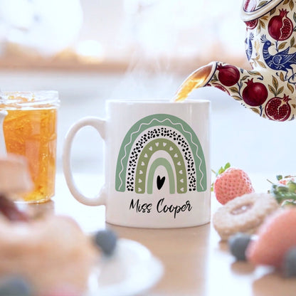 Mug with a rainbow design and 'Miss Cooper' text, being filled with tea.