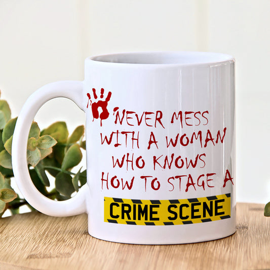 White mug with red and black text and a yellow warning label on a wooden surface with a plant in the background