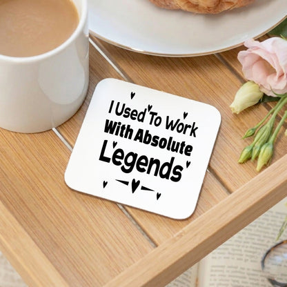 I Used To Work With Absolute Legends' white glossy coaster displayed on a wooden tray alongside a cup of tea, a croissant, and pink flowers