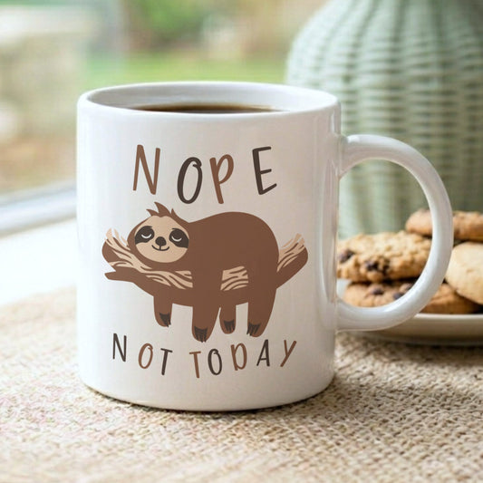 'Nope Not Today' sloth mug filled with coffee, displayed on a jute mat on a windowsill with a plate of cookies and a sage green vase
