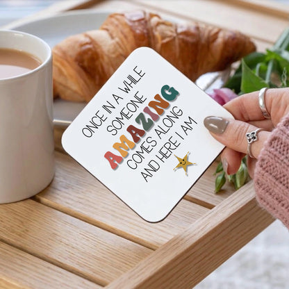 Coaster with motivational quote held by a hand on a table with coffee and croissant