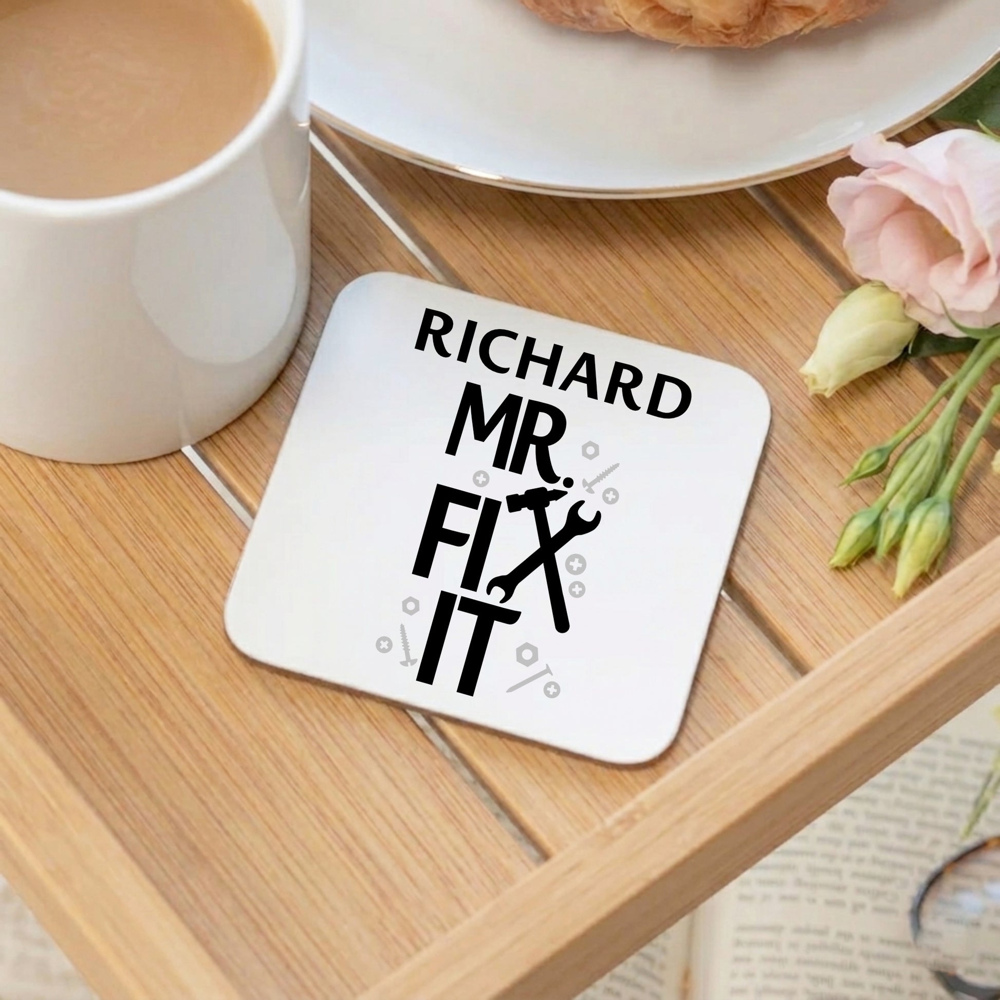 Coaster with 'Richard Mr. Fix It' text on a wooden table with a mug and flowers.