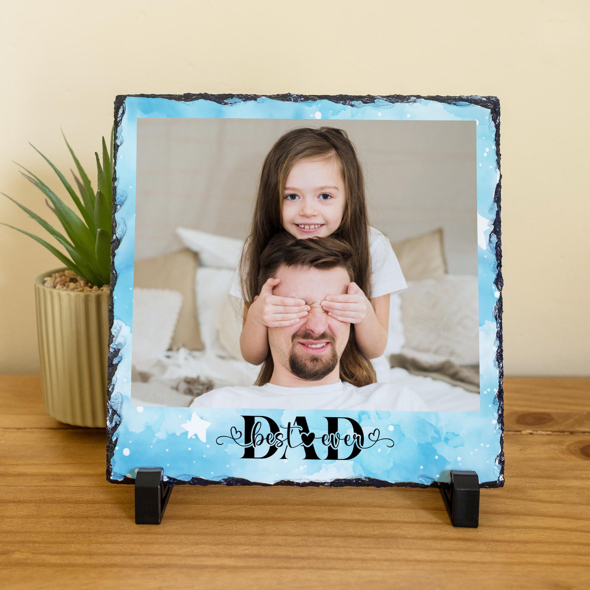 Personalised Best Ever Dad photo slate with blue watercolour background, showing a daughter sitting on dad's shoulders covering his eyes, with two black display stands