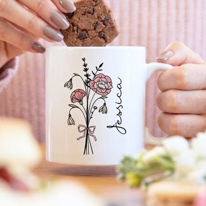 Person holding a mug with floral design and 'Jessica' text, eating a cookie.