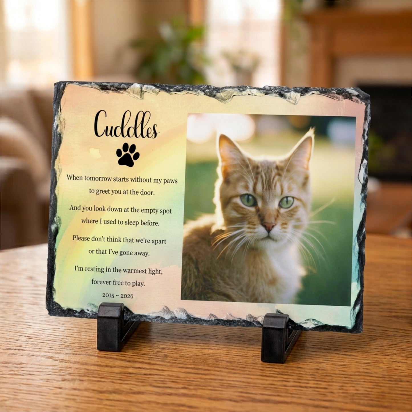 Personalised pet memorial plaque on a black display stand, featuring a photo of a cat and a comforting poem with the name 'Cuddles' and a paw print, displayed on a wooden surface.
