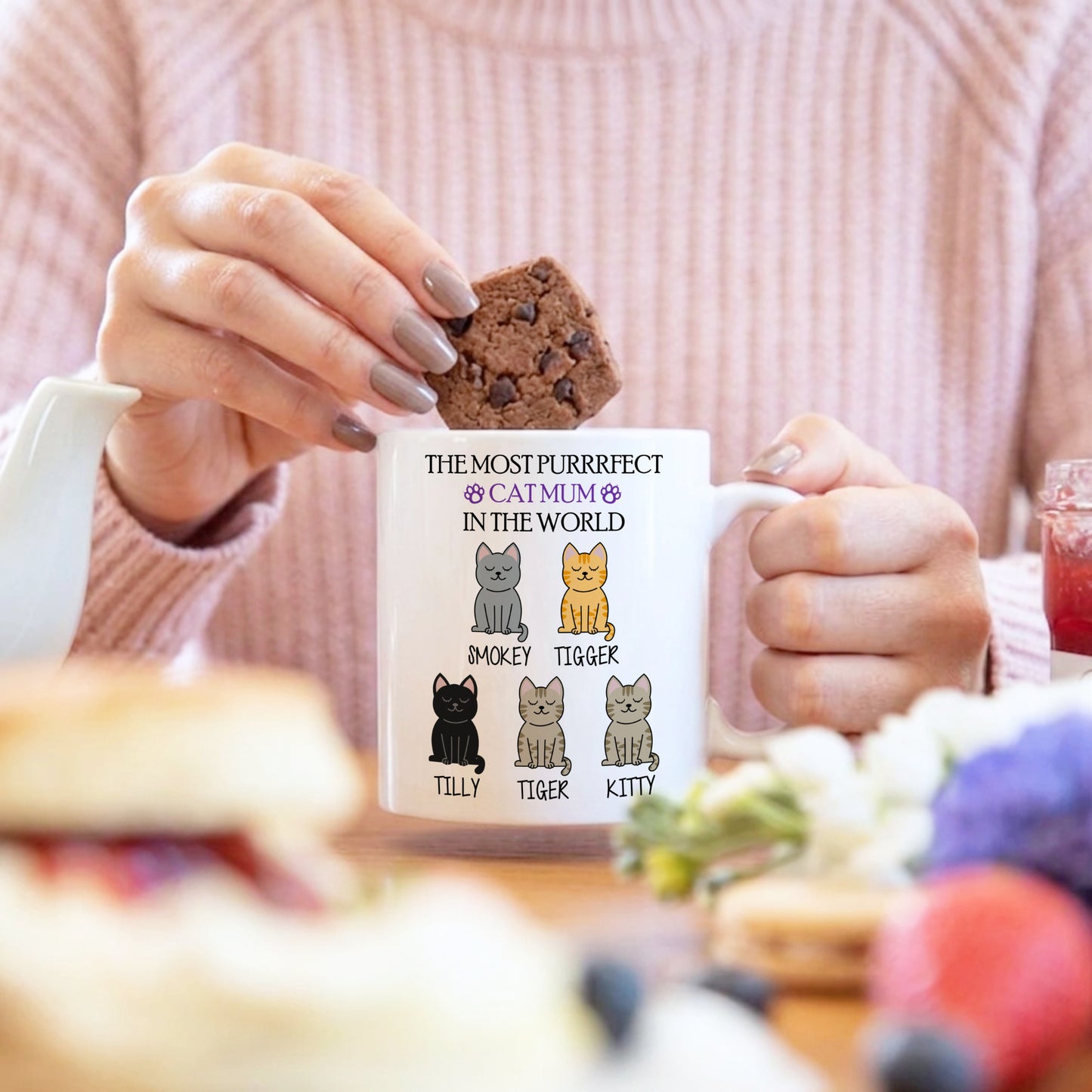 Person holding a mug with cat illustrations and text, sitting at a table with food.