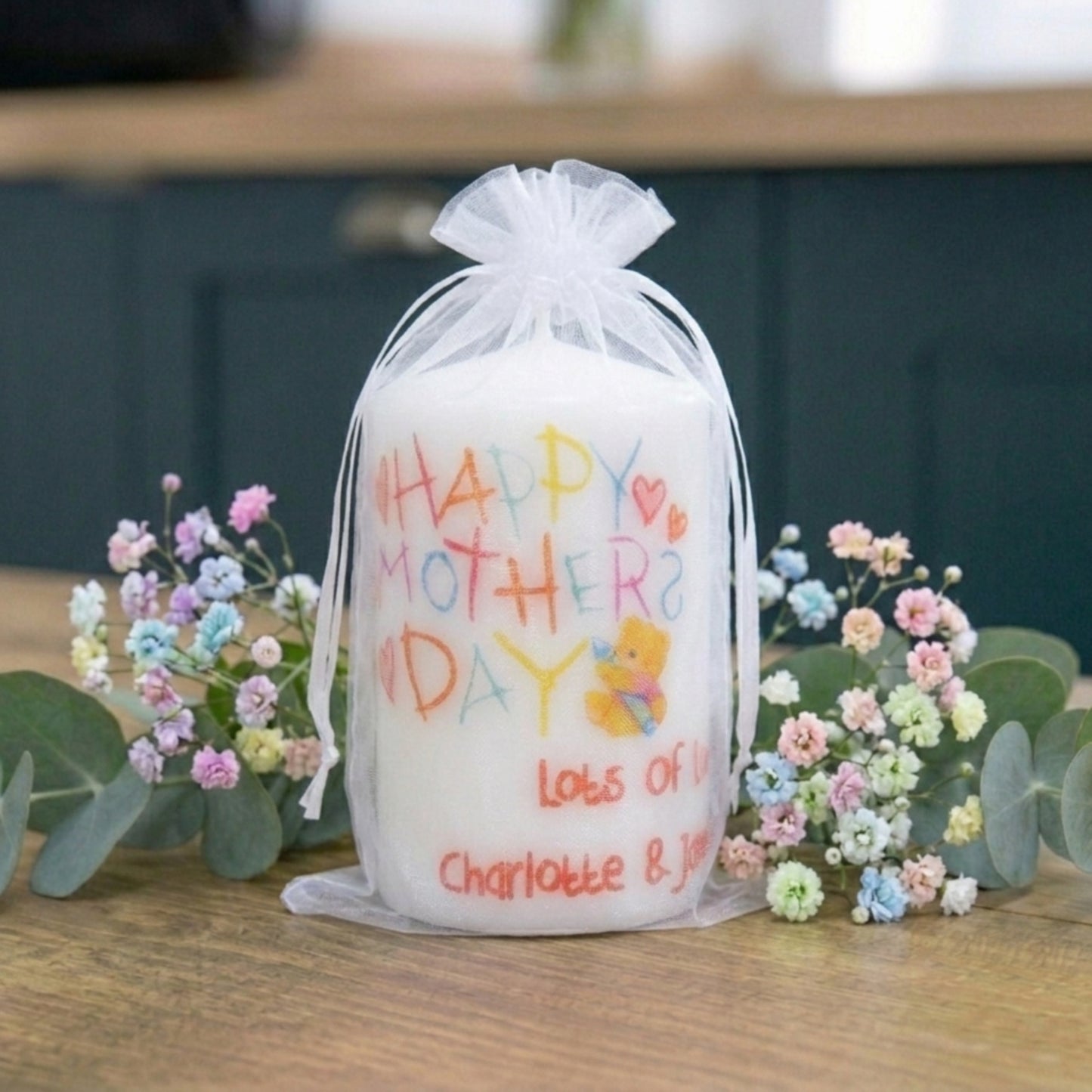 Candle with 'Happy Mother's Day' message and flowers on a wooden surface