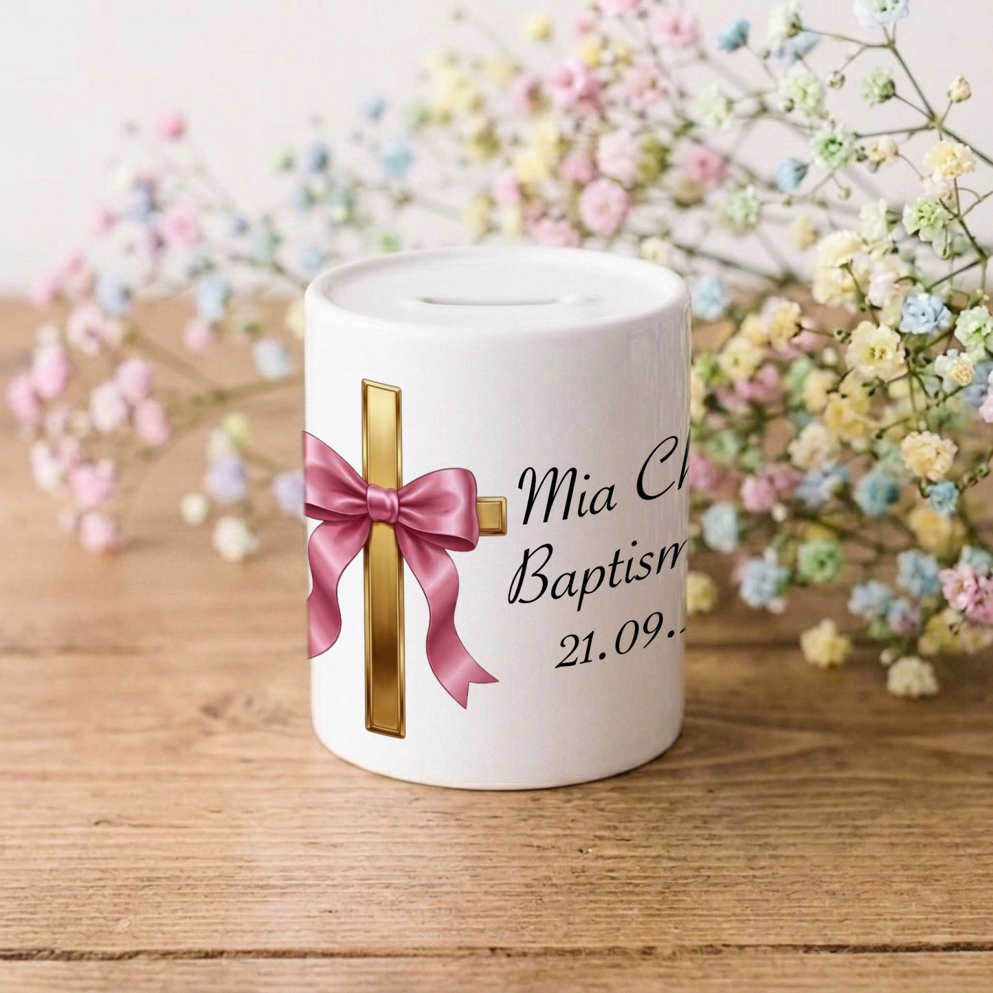 A white ceramic baby baptism money box with a gold cross, pink satin bow, and printed black text reading 'Mia C Baptism 21.09.