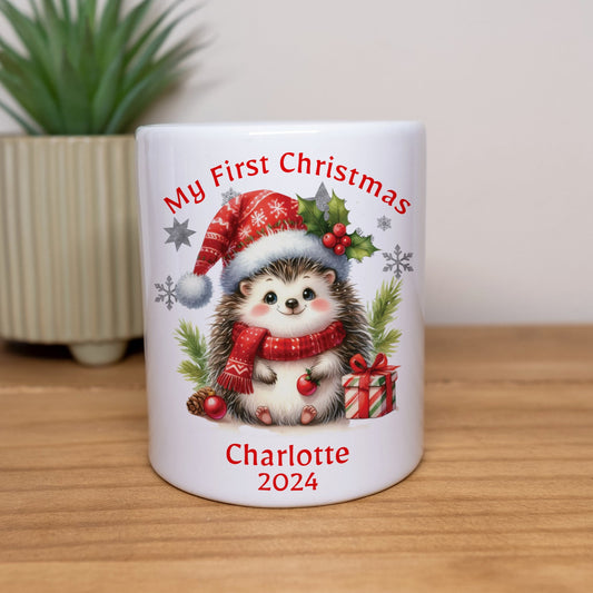 White mug with a hedgehog design and text 'My First Christmas Charlotte 2024' on a wooden surface.