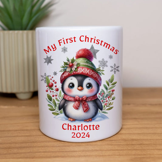 White mug with a penguin design and text 'My First Christmas Charlotte 2024' on a wooden surface.