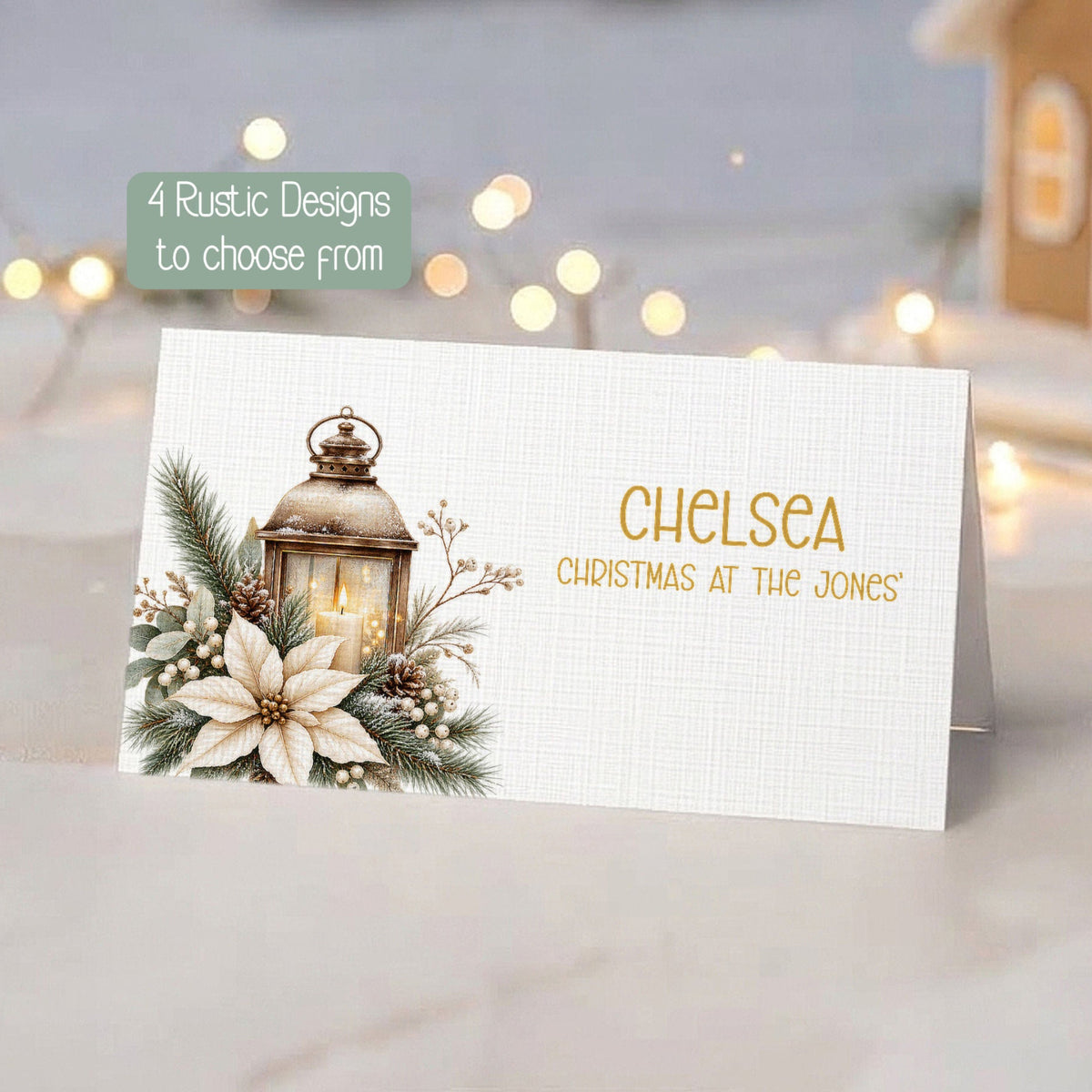 A personalised Christmas place card with a rustic design, featuring a watercolour lantern, white flowers, and green pine branches on a white textured cardstock. The card is displayed on a marble surface with a blurred holiday background containing warm string lights and a gingerbread house.