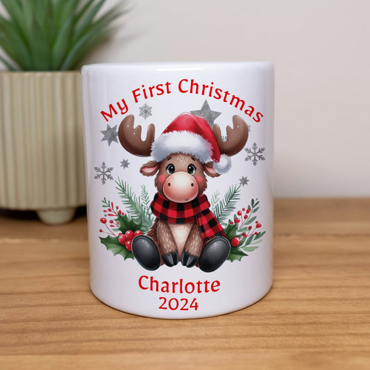 Mug with a reindeer design and text 'My First Christmas Charlotte 2024' on a wooden surface.