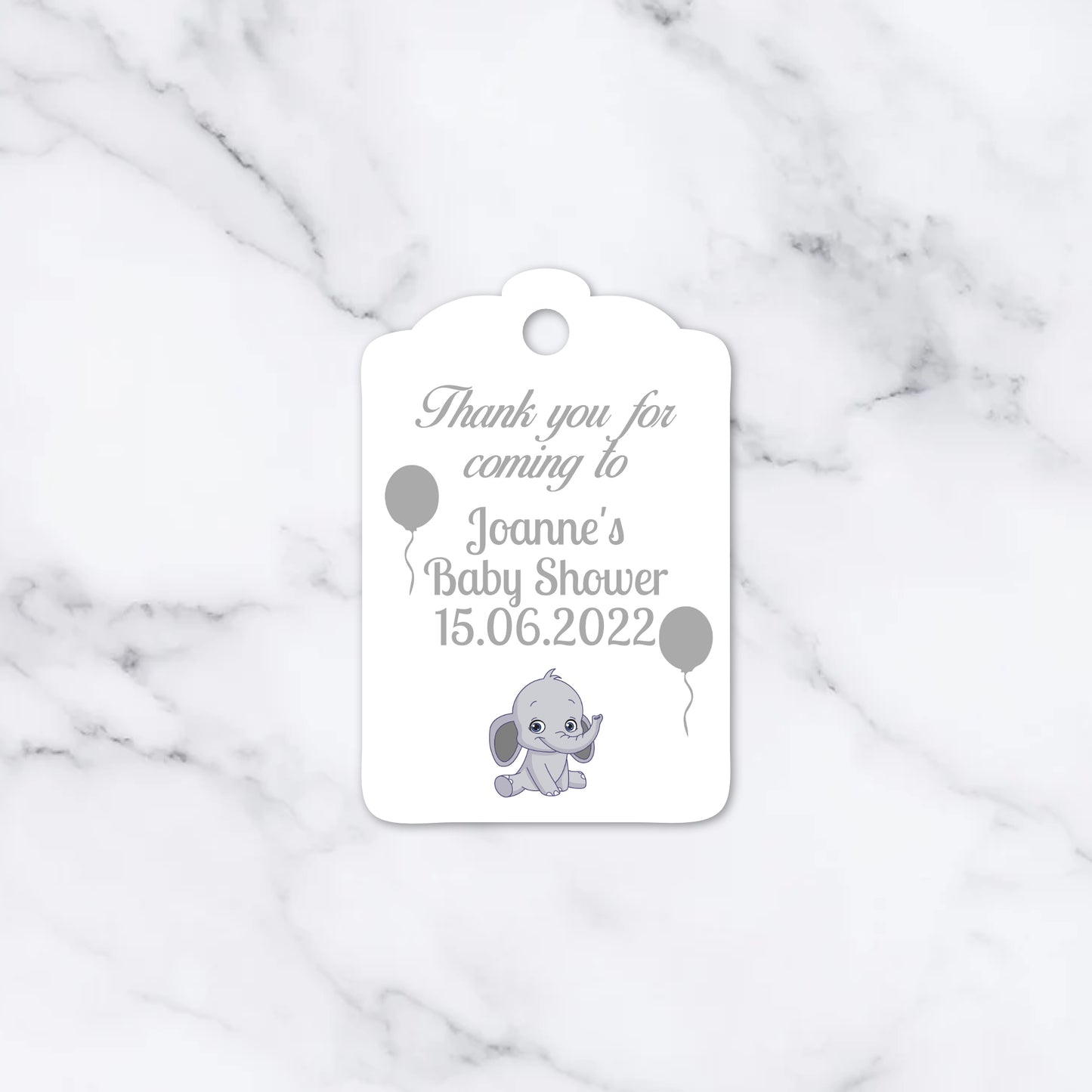 A white personalised baby shower thank you tag with a scalloped top edge, featuring a grey elephant illustration, balloons, and printed text on a white marble background.