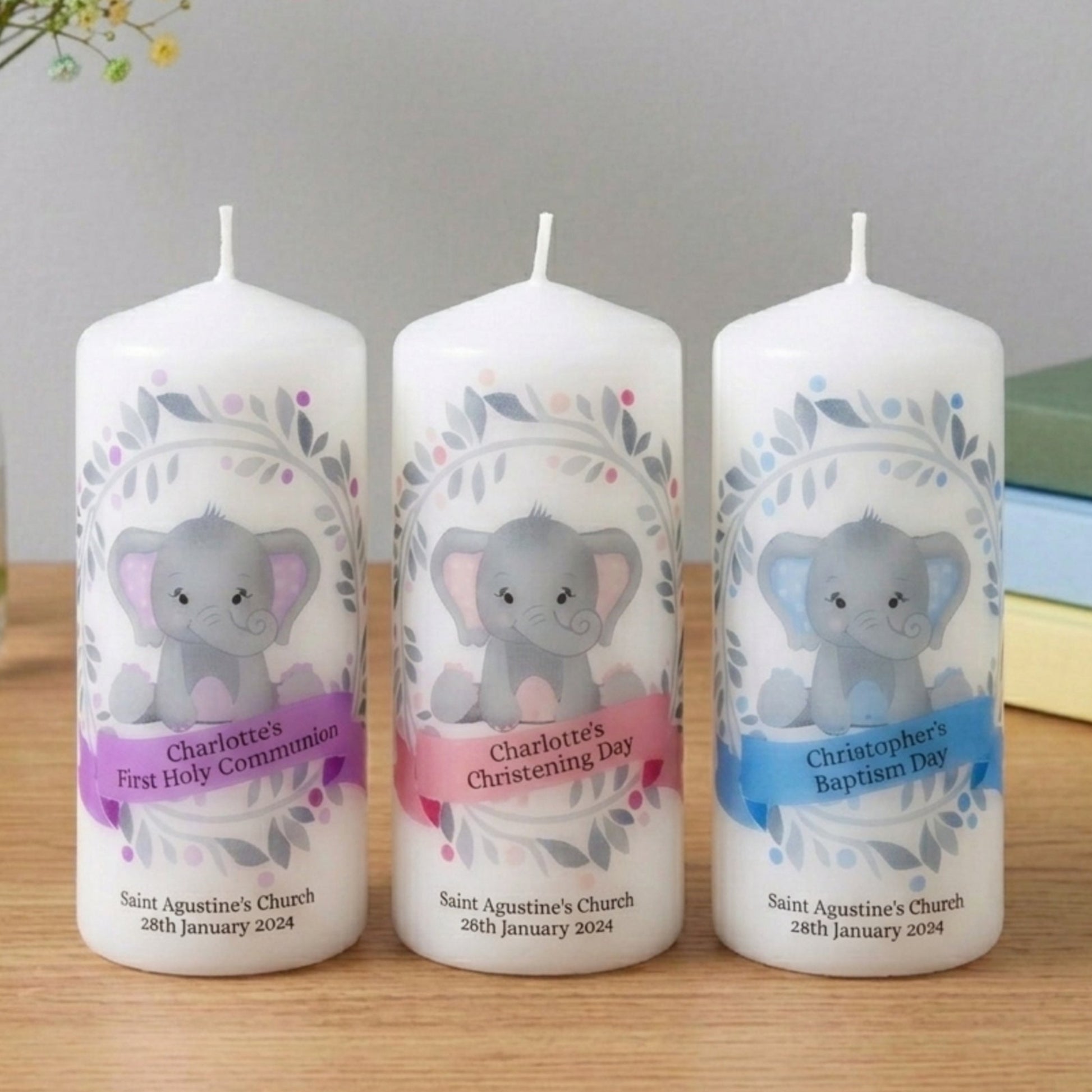 Three personalized candles with elephant designs on a wooden surface.