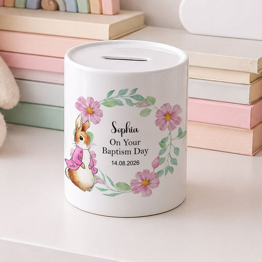 A white cylindrical baptism money box with a floral and bunny illustration, personalised with the name 'Sophia' and the text 'On Your Baptism Day 14.08.
