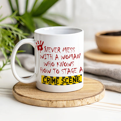 A white ceramic mug with a humorous crime scene-themed quote in red text and a yellow caution tape graphic, displayed on a round wooden coaster with a blurred kitchen background.