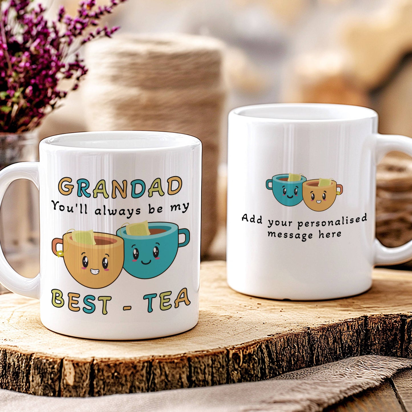 Two white ceramic mugs displayed on a rustic wood slice. The mug on the left is personalised with the text 'GRANDAD You'll always be my BEST - TEA' and features two smiling cartoon cups.