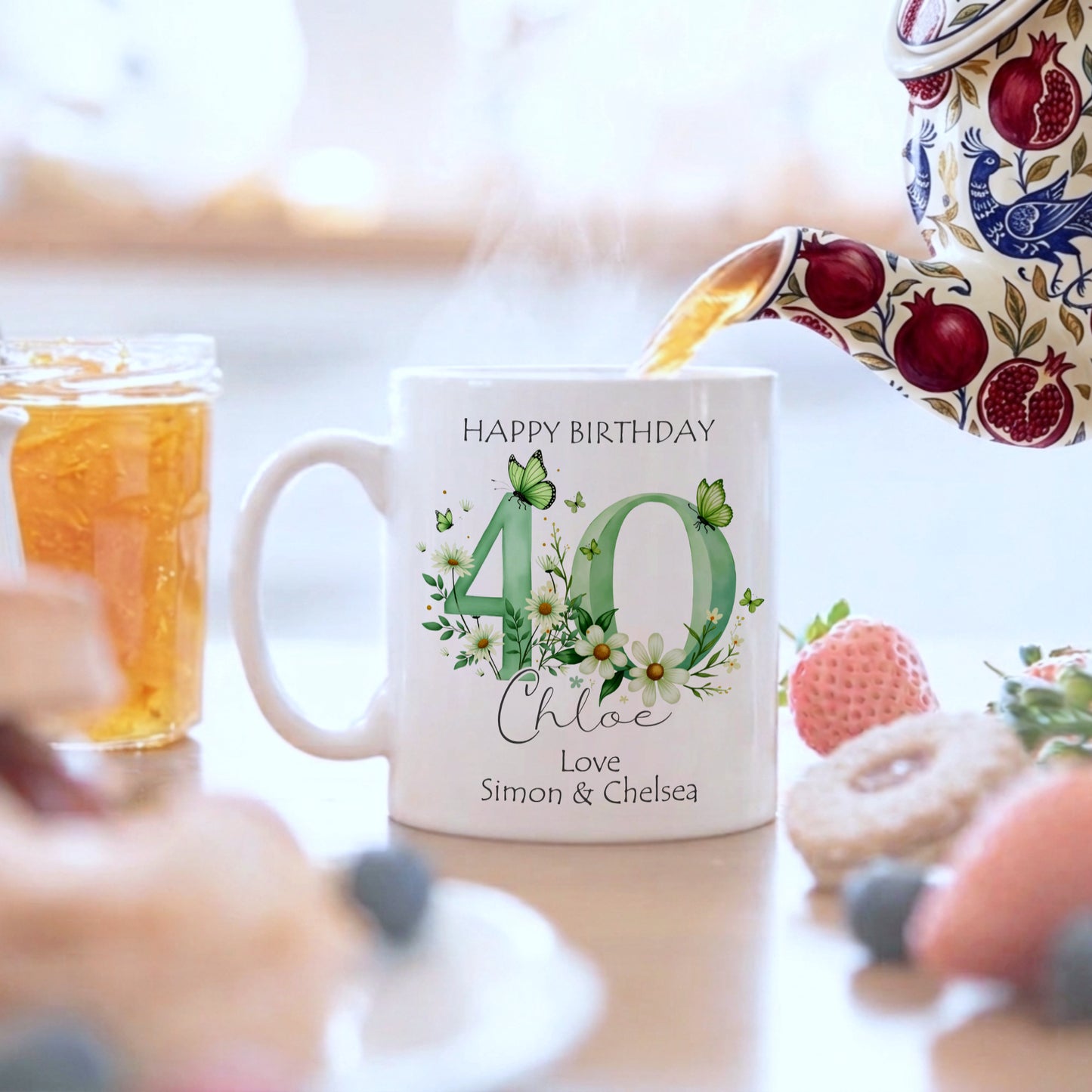 Personalized birthday mug with floral design and text, surrounded by a blurred background of a table with food and drinks.