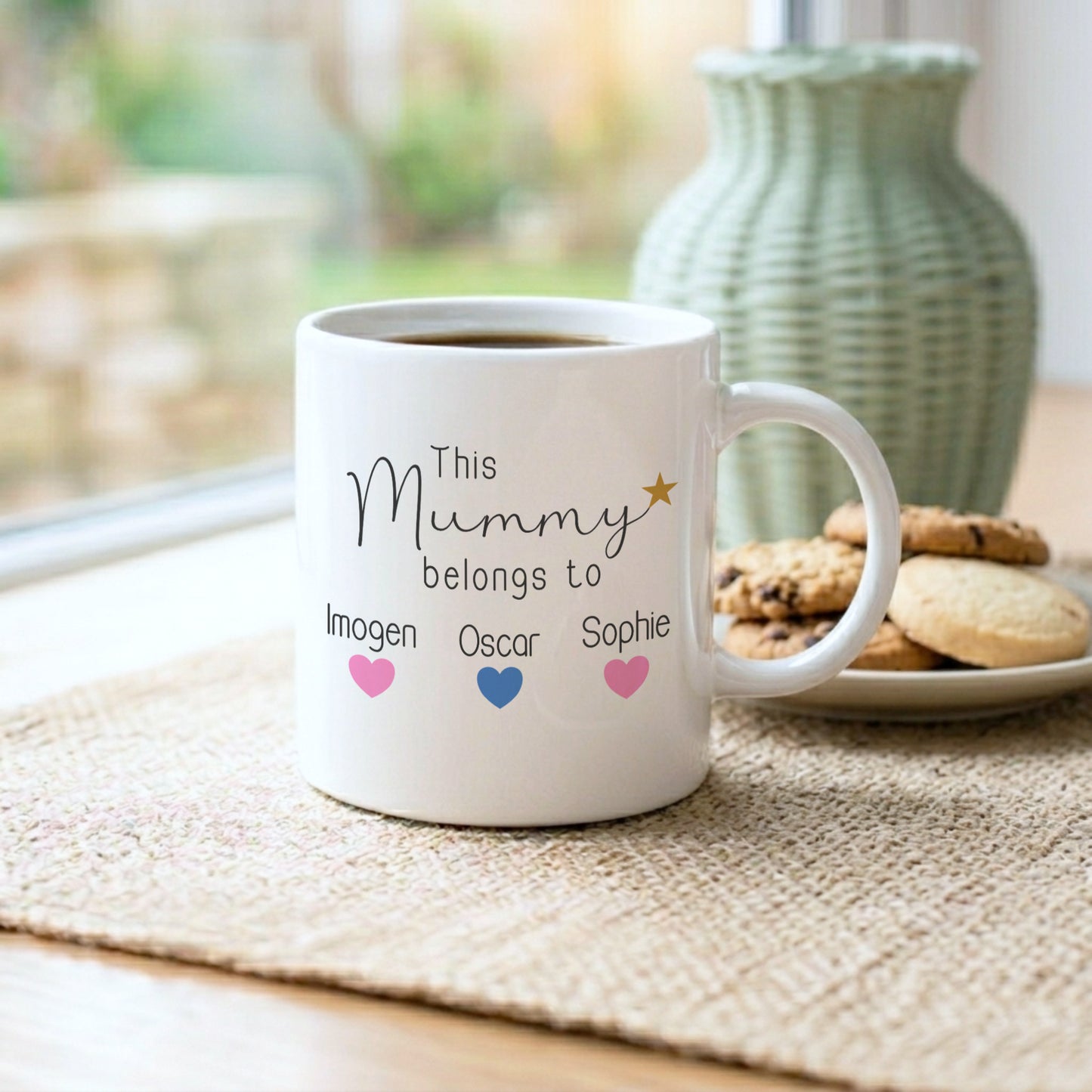 White mug with personalized text on a table with cookies and a vase in the background
