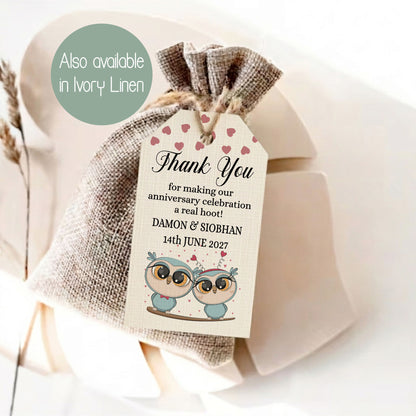 A burlap drawstring gift bag tied with twine, featuring a printed thank-you tag with pink hearts and cartoon owl illustrations. A green circular callout reads 'Also available in Ivory Linen.