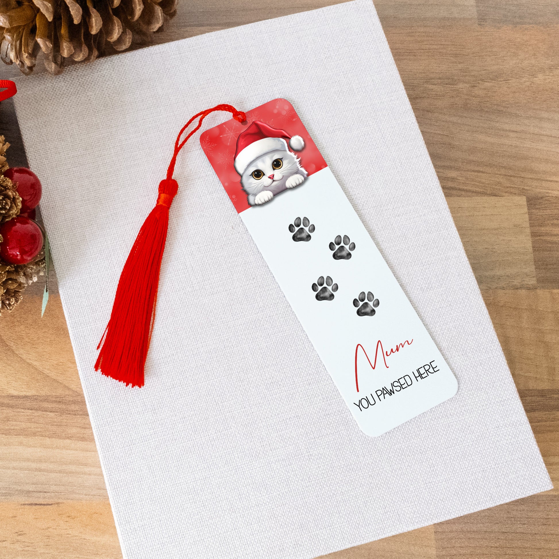 Bookmark with a cat design and tassel on a white card, surrounded by decorative items on a wooden surface.