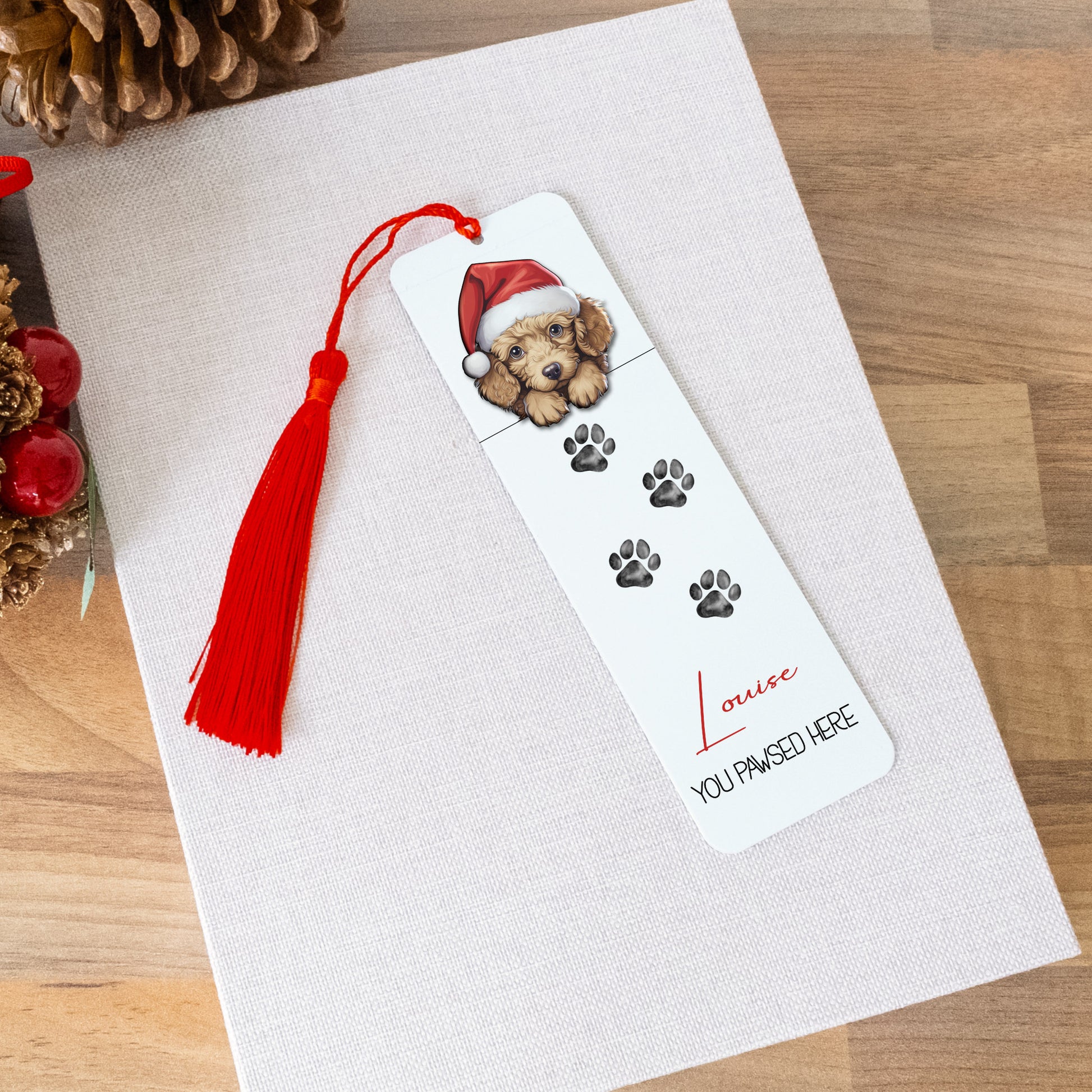 Bookmark with a dog wearing a Santa hat on a white card with red tassel, surrounded by Christmas decorations.