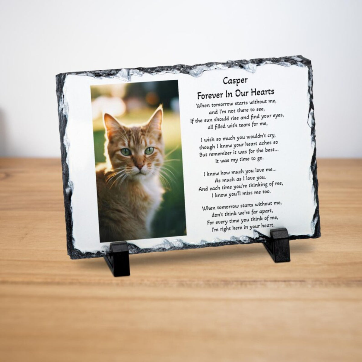 A personalised memorial slate plaque on a small black stand, featuring a photo of an orange tabby cat and the text 'Casper Forever In Our Hearts' with a poem. The plaque is displayed on a light wooden surface against a white background.