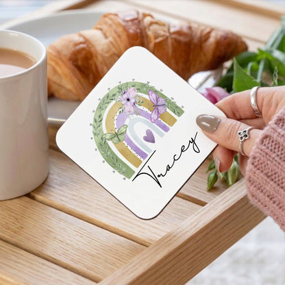 Coaster with floral design and name 'Tracey' held by a hand on a table with coffee and croissant.