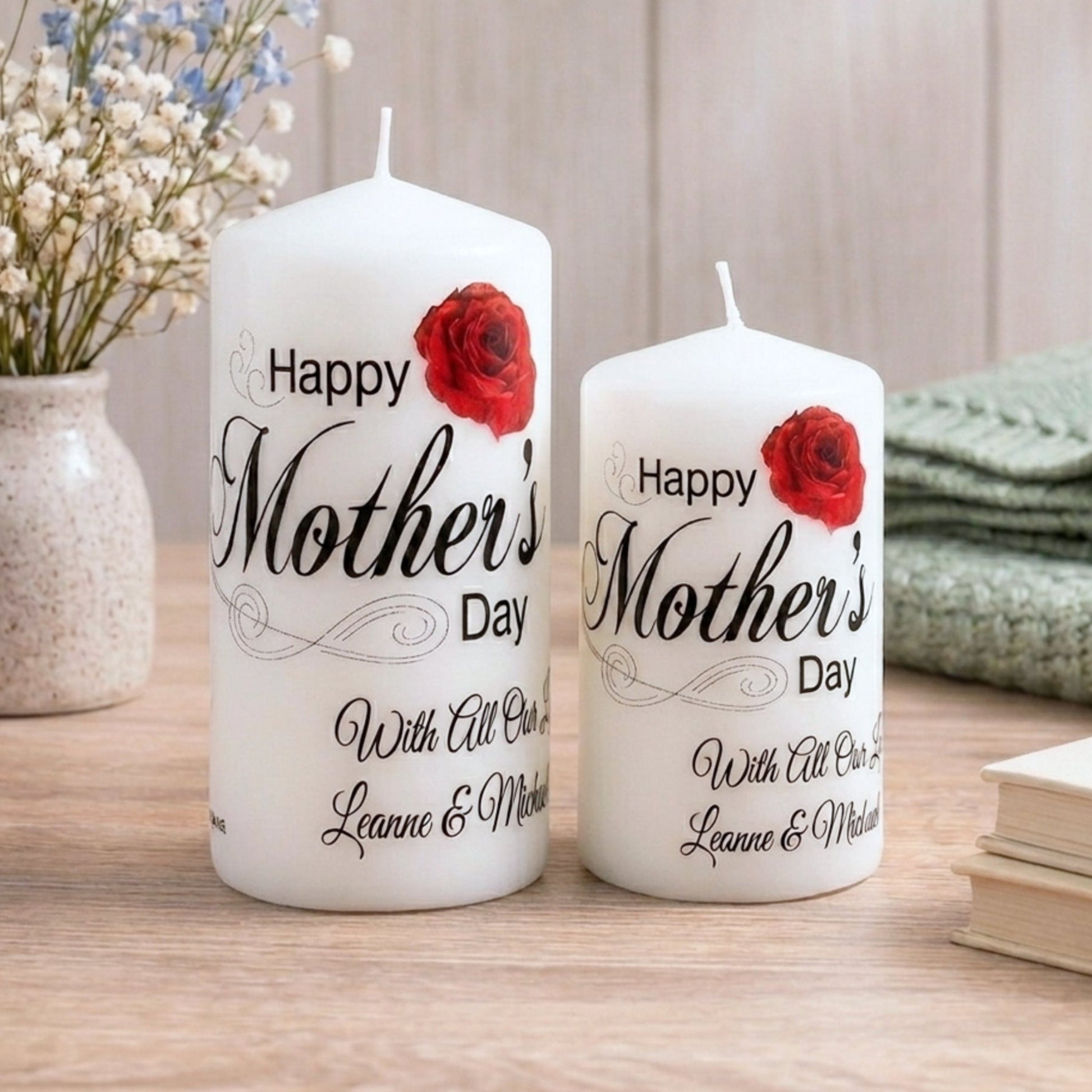 Two white candles with 'Happy Mother's Day' text and red roses on a wooden surface.