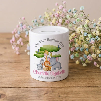 Personalised baptism money box with cartoon animals on a wooden surface with flowers in the background