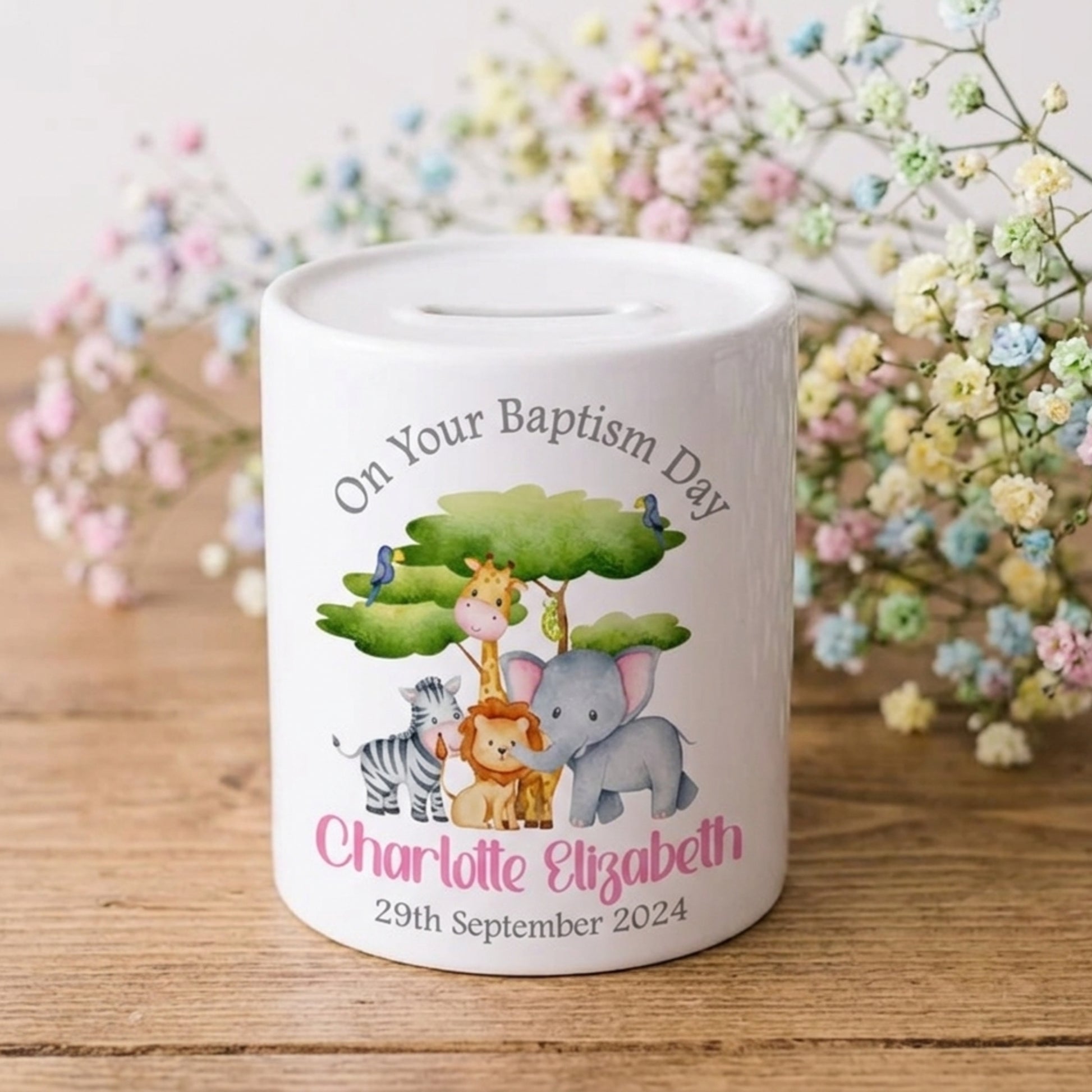 Personalised money box with animal illustrations and text on a wooden surface with flowers in the background