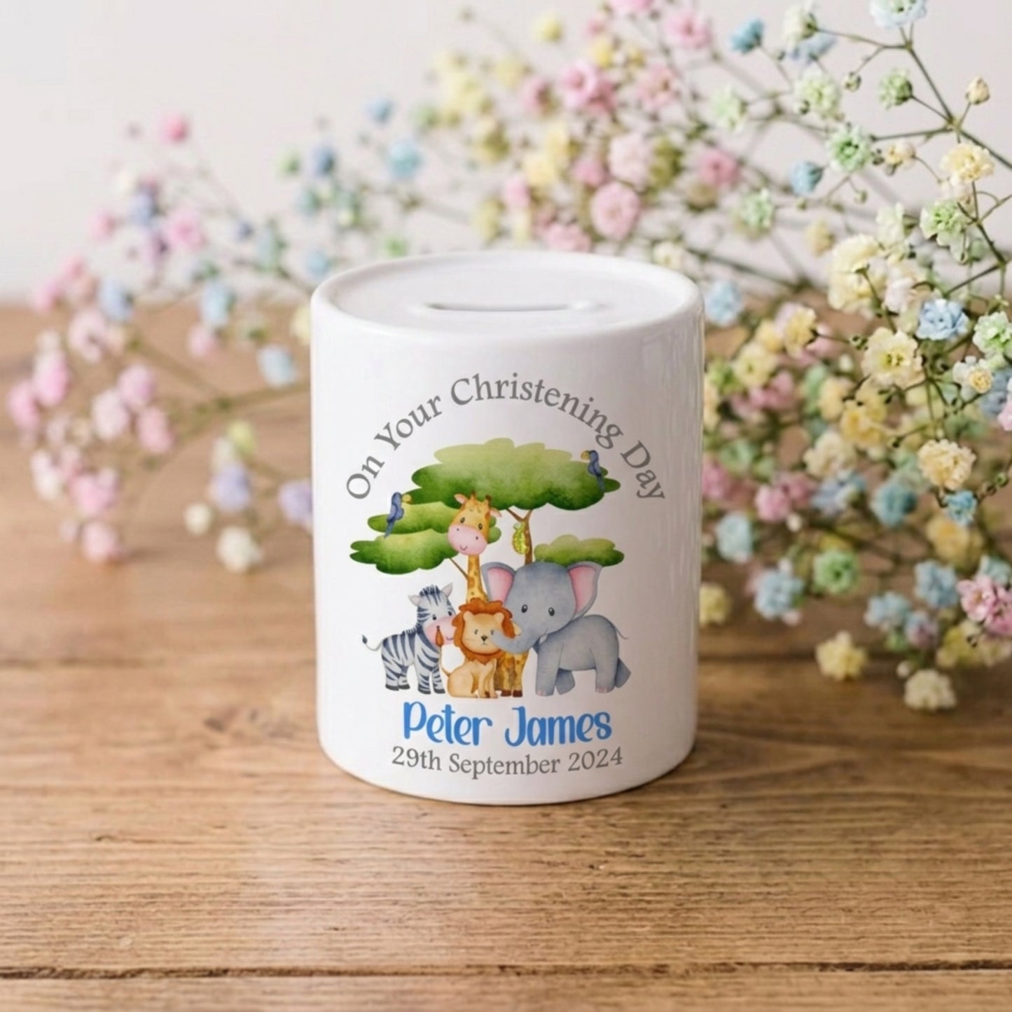 Personalised money box with cartoon animals on a wooden surface with flowers in the background