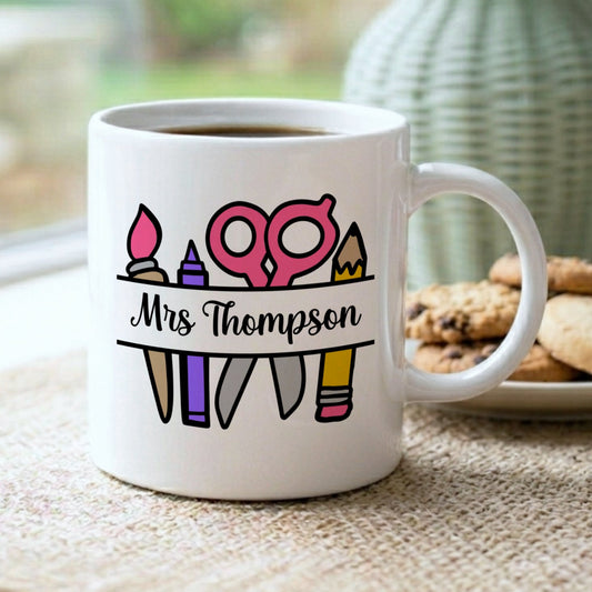 White mug with colorful teacher-themed design and 'Mrs. Thompson' text on a table with cookies and a vase.