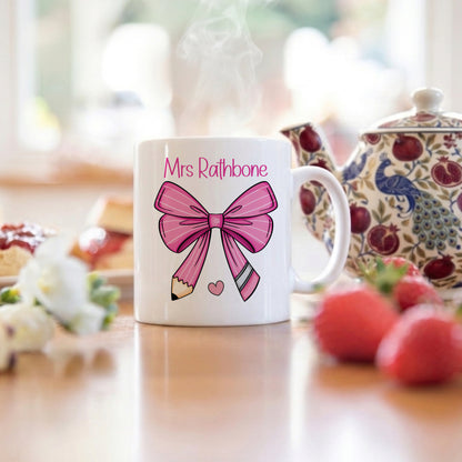 White mug with pink bow design and 'Mrs. Rathbone' text on a blurred background of a kitchen.