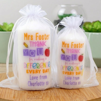 Two personalised candles with printed text 'Mrs Foster THANK YOU for making a DIFFERENCE every day' with additional personalized text that reads 'Love from Charlotte xx'. The candles are placed in transparent packaging.